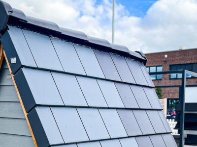 Dachmodell mit grauen Ziegeln unter wolkigem Himmel, zeigt Materialien f&uuml;r Dachdeckung im Au&szlig;enbereich.