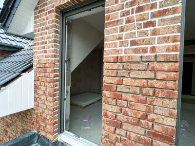 Offene T&uuml;r f&uuml;hrt in unfertigen Raum mit Ziegelw&auml;nden, zeigt Baufortschritt im Rohbau eines Geb&auml;udes.